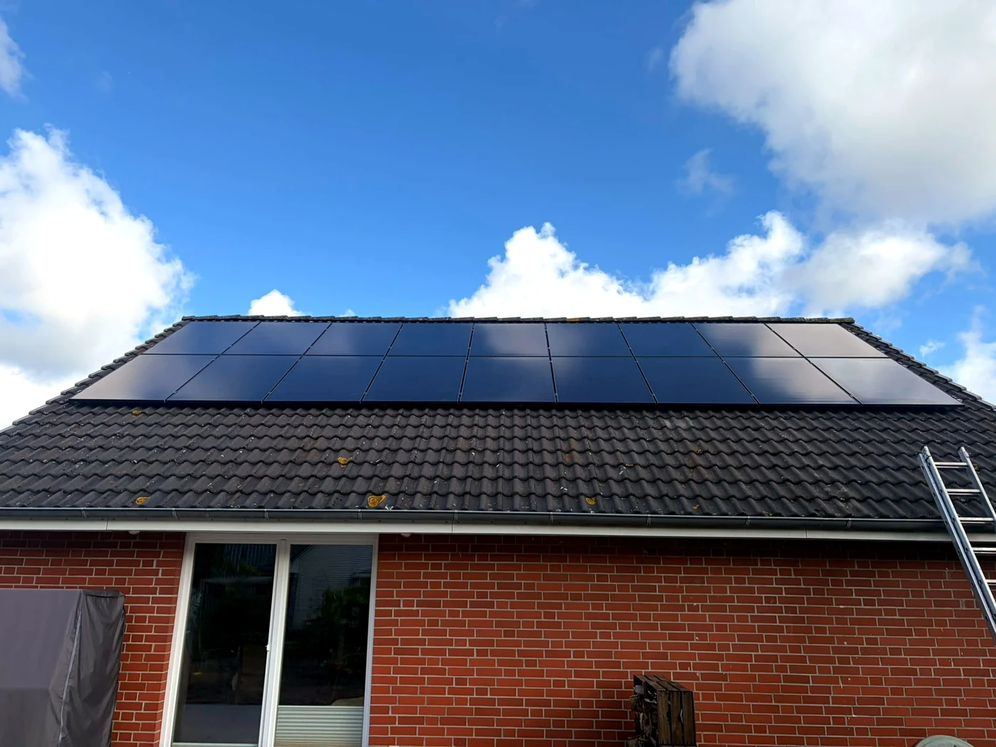 Schwarze Photovoltaikmodule auf dem Ziegeldach eines Backsteinhauses